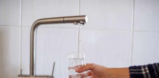 Hand filling a glass with water from a kitchen faucet