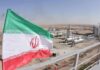 Iran flag over an oil and gas facility in a desert landscape