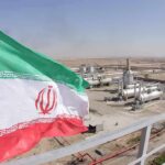 Iran Draws Line—Not A Word Till 2029 Iran flag over an oil and gas facility in a desert landscape