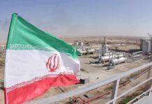 Iran Draws Line—Not A Word Till 2029 Iran flag over an oil and gas facility in a desert landscape