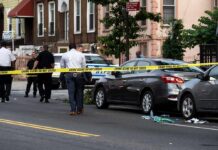 Police at urban street crime scene with yellow tape around parked cars