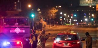 Security officers stop a red taxi at a night checkpoint