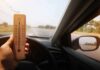 Hand holding a wooden thermometer inside a car on a sunny road