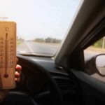 Hand holding a wooden thermometer inside a car on a sunny road