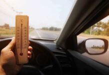 France’s Hottest July Breaks Records Hand holding a wooden thermometer inside a car on a sunny road