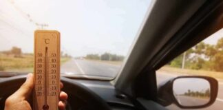 Hand holding a wooden thermometer inside a car on a sunny road