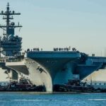 War Bills Blow Hole In Navy Budget Aircraft carrier guided by tugboats in a harbor