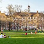 Two Deaths, One Mystery: Campus On Edge Students relaxing on a campus quad in front of a brick academic building