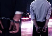 Two men in handcuffs with police lights in the background