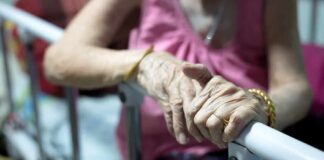 Elderly person’s hands resting on a hospital bed rail