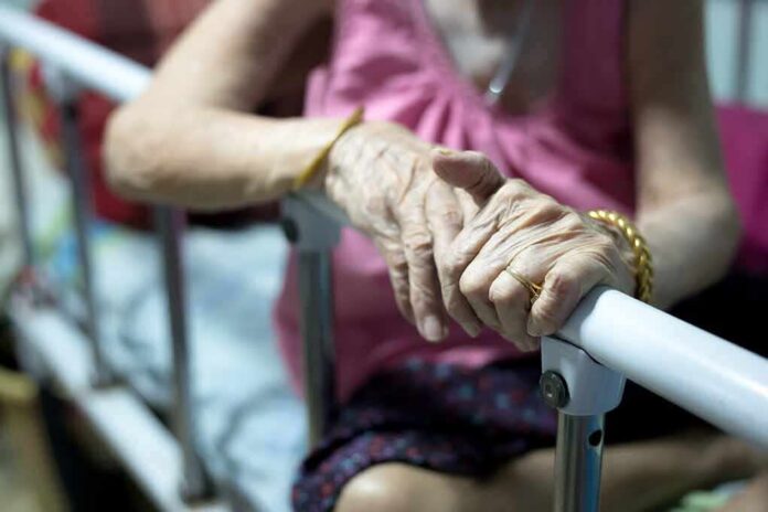 shutterstock_1048637588 Elderly person’s hands resting on a hospital bed rail