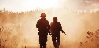 Two soldiers walking through a smoky field at sunset