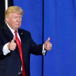 Trump’s Arch Goes Military? Donald Trump giving two thumbs up in front of a blue curtain