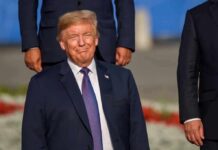 Trump – NYC Deal Talk Teases Big Build smiling man in a navy suit at an outdoor event