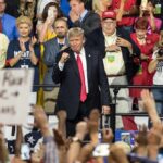 GOP Allies Put Affordability At Center Of Midterms politician on stage at a rally raising a fist amid cheering crowd