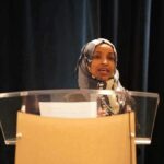 Republicans Bristle As Omar Recasts Billions Woman in hijab speaking at a podium