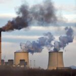 Grid Relief Or Health Disaster? Industrial power plant with smokestack and cooling towers emitting smoke