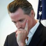 Newsom Claims Slammed By His Own Numbers man in suit touching his face thoughtfully