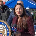 2028 Rumors Swirl After AOC Move Woman speaking at outdoor press event with microphones and seal