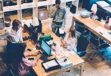 Layoffs Hit, AI Grabs the Bylines Four coworkers collaborate at shared desks in a modern office