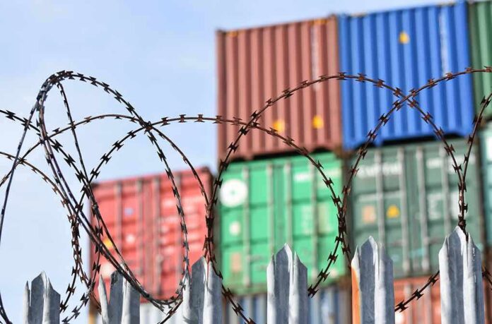 Barbed wire fence in front of stacked shipping containers