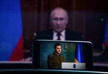 UN Showdown: Zelenskyy Demands Pain For Putin Vladimir Putin blurred in background behind smartphone showing a speech