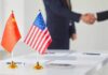 Xi – Trump Deal Teases Price Relief Chinese and American flags on a table with a handshake in the background