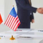 Chinese and American flags on a table with a handshake in the background