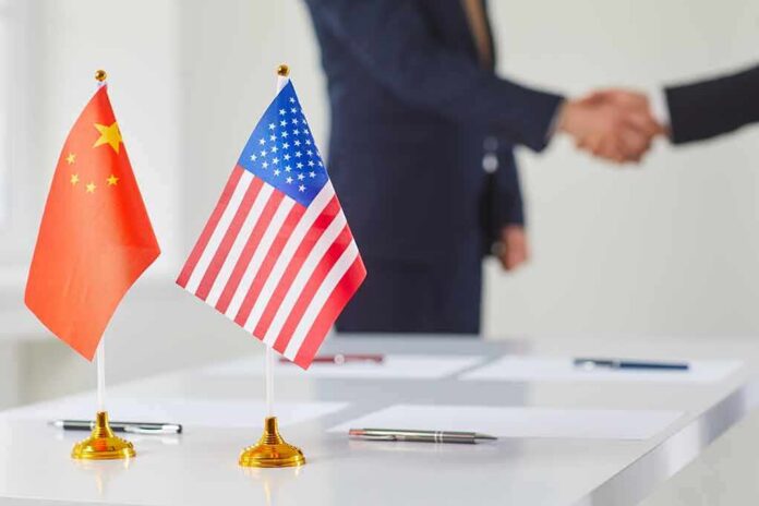 Chinese and American flags on a table with a handshake in the background