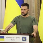 Ukraine Demands Guarantees Before Halting Strikes Man at a podium with Ukrainian flags