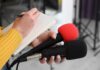 Journalist holding two microphones while writing in a notebook