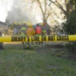 Bat-Swinging Fugitive Terrifies Quiet Town Yellow police tape marking a restricted area at a fire scene with firefighters in the background