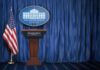 Early Mic Drop: Trump’s Messenger Arrives White House press briefing podium with U.S. flag and blue curtain