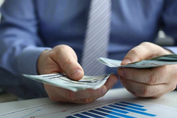 shutterstock_1291795882 Hands counting cash over financial documents