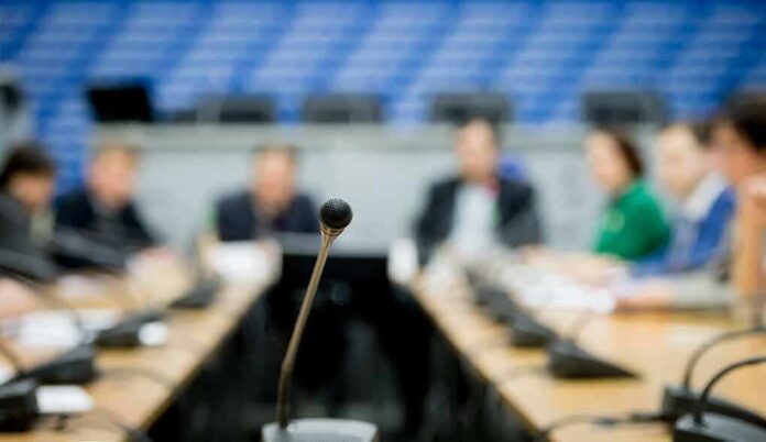 shutterstock_1305479749 Caraun Reid at a conference table with a microphone in focus