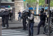 Riot police in helmets line a city street during an operation