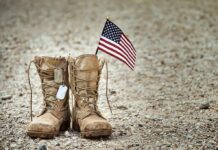 Trusted Insider Drains Disabled Vets’ Cash Combat boots with dog tags and a small American flag on gravel