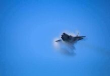 fighter jet creating vapor cone in blue sky