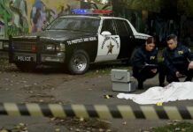 City Employee Linked To Cop Ambush Crime scene with police car and two investigators by a covered body
