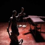 Execution Drama Returns To Texas Lady Justice statue with scales in dramatic light beside an empty gurney