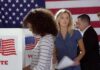Voters at polling booths in front of an American flag
