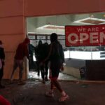 Shops Smashed As Protests Boil Over People outside a storefront with broken glass at night