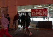 Shops Smashed As Protests Boil Over People outside a storefront with broken glass at night