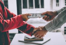 Two people exchange cash while shaking hands