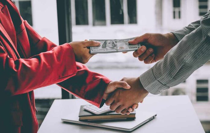 Two people exchange cash while shaking hands