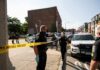 Daylight Raid Turns Chaotic In NYC Police officers secure an urban street with yellow tape near patrol cars