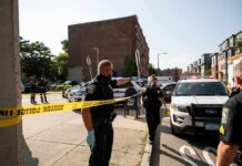 Daylight Raid Turns Chaotic In NYC Police officers secure an urban street with yellow tape near patrol cars