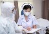 nurse in PPE writing on a clipboard with colleague