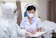 nurse in PPE writing on a clipboard with colleague