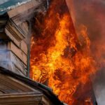 Evacuations Race Ahead of Firestorm House on fire with flames pouring from a window